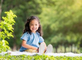 niña asiática sentada en la alfombra, relajándose y aprendiendo fuera de la escuela para disfrutar en el parque natural foto