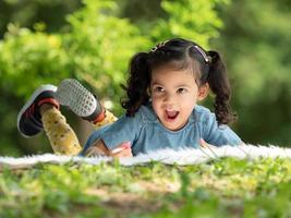 An Asian girl is lying on the carpet and painted with crayons, Which is fun learning outside the school in the nature park photo