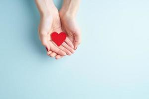person holding red heart in hands, donate and family insurance concept, on aquamarine background photo