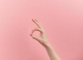 Woman hand shows ok symbol on pink pastel background with copy space