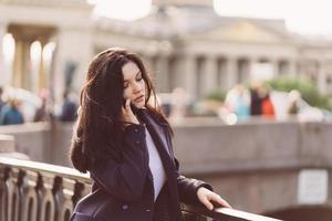 Woman with long hair talking on phone. Autumn or winter, girl in outdoor. Beautiful intelligent brunette in street of St. Petersburg in city center near bridge photo