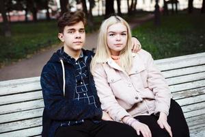 los adolescentes enamorados se sientan en un banco del parque en otoño y miran al frente foto