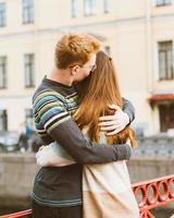 red-haired man kisses a woman on the top of her head, a boy in a sweater soothes and comforts a girl with long dark thick hair photo