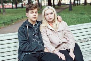 Teenagers in love sit on park bench in autumn, looking straight ahead. Concept of teen love photo