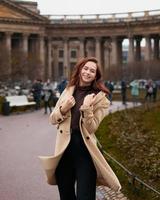 Beautiful funny naughty stylish fashionable happy girl dancing on streets of St. Petersburg city. Charming smiling woman with long dark hair, vertical photo