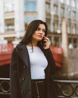 Woman with long hair talking on phone. Autumn or winter, girl in outdoor. Beautiful intelligent brunette in street of Saint-Petersburg in city center near bridge, copy space