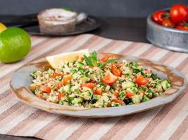 Tabbouleh salad with quinoa. Eastern food with vegetables mix, vegan diet. Side view, linen napkin, old plate
