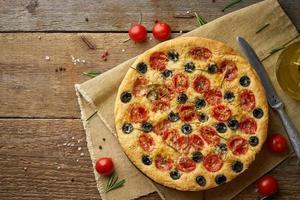 Focaccia, pizza, italian flat bread with tomatoes, olives and rosemary on wooden rustic table, copy space