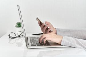 mujer irreconocible que usa un teléfono inteligente mientras escribe en una computadora portátil, concepto de entrada de contraseña