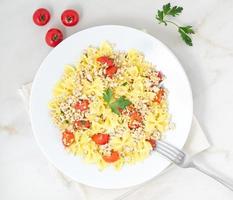 farfalle pasta with tomatoes, chiken meat, parsley on white stone background, low-calorie diet, top view photo
