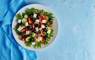 Greek salad on white plate on bright blue table, top view, copy space photo