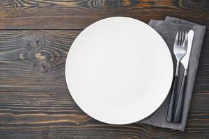 clean empty white plate, fork and knife on dark rustic wooden table, copy space, mock up, top view. photo