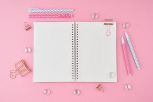 Blank notepad page in bullet journal on bright pink office desktop. Top view of modern bright table with notebook, stationery. Mock up, copy space, concept for diary