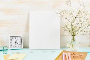 Mockup with blank white frame on blue table against wooden wall, alarm, flower in vaze photo