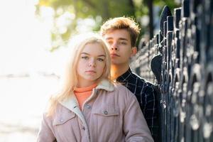 A man gently hugs a woman, a guy and a girl are close to fence of Park, looking forward. The concept of first teenage love and first kiss. A boy with dark hair and girl blonde Scandinavian photo