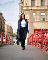 Charming thoughtful fashionably dressed woman with long dark hair travels through Europe, walking in the city center of St. Petersburg. A beautiful girl wanders alone through autumn streets photo