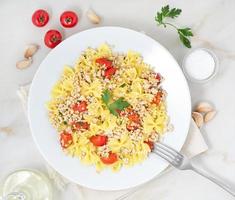 farfalle pasta with tomatoes, chiken meat, parsley on white stone background, low-calorie diet, top view photo