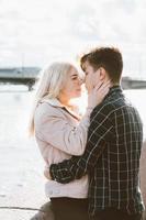 The boy looks tenderly at girl and wants to kiss. A young couple stands embracing. The concept of teenage love and first kiss, sincere feelings of man and woman. The city, the waterfront. Vertical