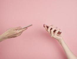 Two women hold phone on pastel pink background copy space side view photo
