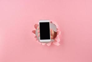 mujer sosteniendo un teléfono inteligente en un agujero envuelto en fondo rosa, espacio de copia