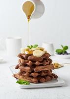 Chocolate banana waffles on white table, vertical. Sweet brunch, maple syrup flow photo