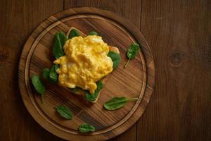 Toast with scrambled eggs and spinach. Omelette. Breakfast with pan-fried eggs on brown dark background. Top view. photo