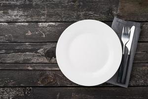 clean empty white plate, fork and knife on gray old rustic wooden table, copy space, mock up