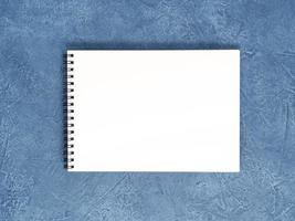 The open notepad with clean white page on aged dark blue stone table, top view photo