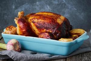 Roasted whole chicken in blue casserole on dark gray old wooden table photo