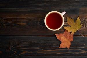 hojas de otoño, taza de té, una mesa de madera oscura. acogedora naturaleza muerta de otoño