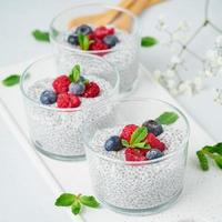 Chia pudding with fresh berries raspberries, blueberries. Three glass, light background, side view, flowers, close up. photo