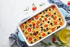 Focaccia with tomatoes, olives and rosemary in casserole, top view, copy space. Italian flat bread photo
