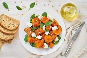 Salad with roasted pumpkin, feta cheese, spinach, nuts with honey and seasonings, top view photo