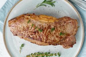 Keto ketogenic diet beef steak, striploin on gray plate on white background. Paleo food photo