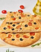 Focaccia, pizza, chopped italian flat bread with tomatoes, olives and rosemary. Vertical, photo