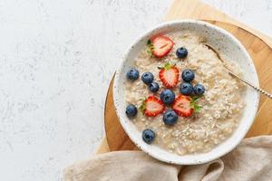 Oatmeal porridge rustic with berries, dash diet, on white wooden background top view photo