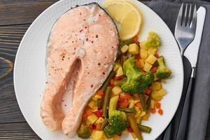 Steam salmon and vegetables, healthy diet. White plate on rustic wooden table, top view, close up photo
