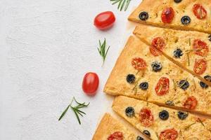 Focaccia, pizza with tomatoes, olives and rosemary. Sliced Italian flat bread photo