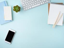 Top view of modern blue office desktop with blank notepad, computer, smartphone. Mock up photo