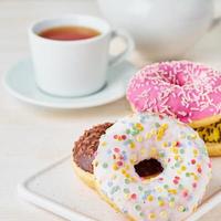 Doughnuts and tea. Bright, colorful junk food. Light beige wooden background. Side view, close up. photo