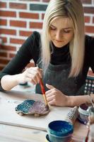 Woman making pattern on ceramic plate with paint brush. Creative hobby concept. Earn extra money, side hustle, turning hobbies into cash, passion into job, vertical photo