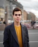 Handsome stylish fashionable man, brunette in elegant gray coat, stands on street in historical center of St. Petersburg. Young man with dark hair, thick eyebrows. photo