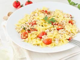 farfalle pasta with tomatoes, chiken meat, parsley on white stone background, low-calorie diet, side view photo