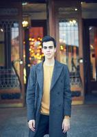 Handsome stylish fashionable man, brunette in elegant gray coat, stands on street in historical center of St. Petersburg. Young man with dark hair, thick eyebrows. photo