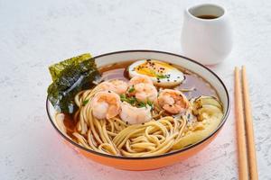 Asian soup with noodles, ramen with shrimps, miso paste, soy sauce. White stone table, side view