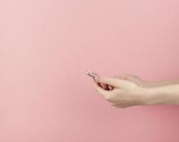 la mano femenina joven sostiene el teléfono inteligente en el espacio de copia de fondo rosa pastel foto