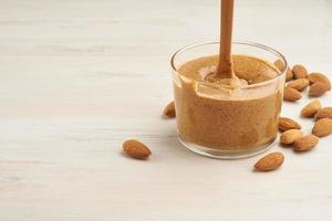 almond butter, raw food paste made from grinding almonds into nut butter, crunchy and stir, white wooden table, copy space photo