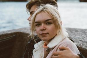 Teenagers in love sit on the waterfront in the city center, resting in autumn sun. Concept the first teenage love, the beginning of relations. A boy and a girl meet on date, couple. Girl close up photo