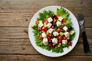 Greek salad on white plate on old rustic wooden table, top view, copy space photo