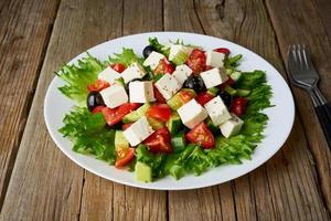 Greek salad on white plate on old rustic wooden table, side view photo